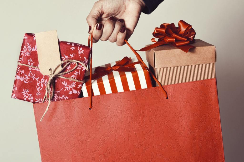 closeup of the hand holding a red shopping bag full of gifts wrapped in different papers