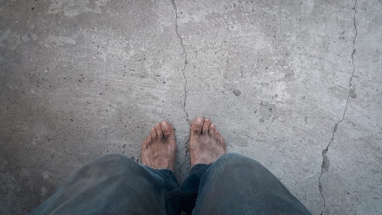 Dirty and bare feet on concrete. A homeless and wandering person. The concept of poverty.