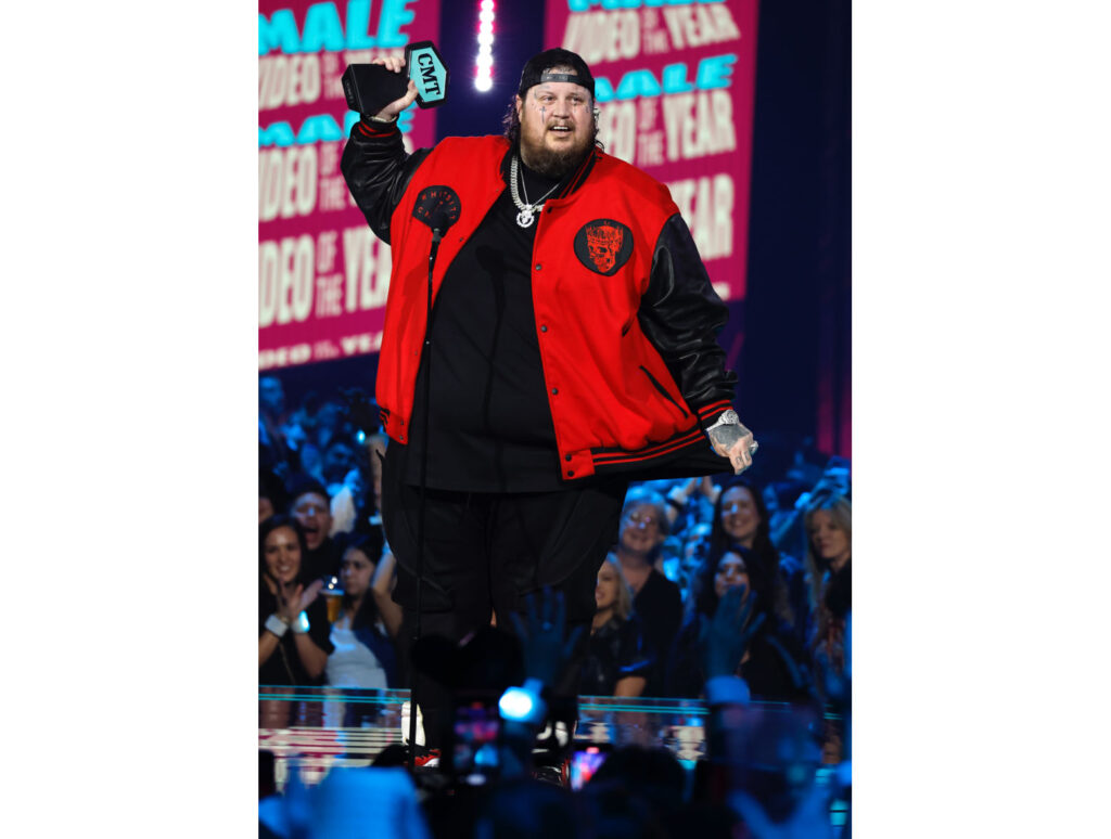 Jelly Roll's Plane Made An Emergency Landing—Jelly was on stage at the 2023 CMT Music Awards wearing a red jacket and ball cap, holding his award. 
